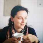 A young woman enjoying a cup of coffee indoors, captured in natural light.